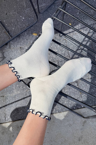 Cream modal ankle socks with navy ruffled trim worn with vintage red leather shoes on outdoor pavement