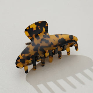Tortoiseshell curved claw clip in amber and black pattern, three-quarter view showing curved design and teeth