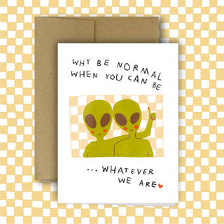 White greeting card with hand-drawn green aliens and text reading 'Why Be Normal When You Can Be Whatever We Are' on checkered background with kraft envelope