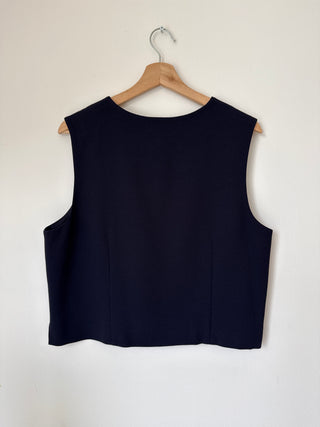 Back view of vintage navy wool vest on wooden hanger displaying clean boat neckline and structured shoulders