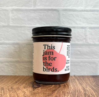 Cherry Apricot jam jar displayed outdoors on wooden fence with text 'Deliciously fight climate change' and green foliage background