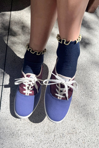Navy blue ribbed ankle socks with cream-colored ruffled trim detail worn with colorblock sneakers on pavement
