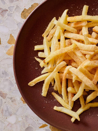 Woon Wok Legend's Seasoning Salt sprinkled on crispy french fries on a dark brown ceramic plate