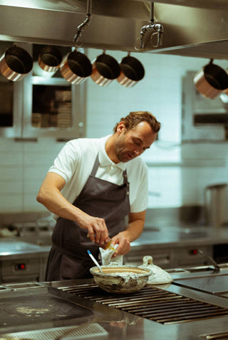Chef Daniel Humm of Eleven Madison Park preparing food in professional kitchen wearing white shirt and dark apron