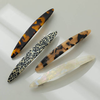 Four vintage oblong oval French barrettes in tortoiseshell, leopard print, and pearl white displayed on white surface