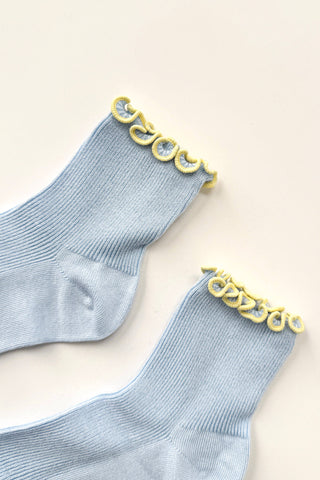 Pair of light blue ribbed modal ankle socks with yellow ruffled trim detail laid flat on beige background