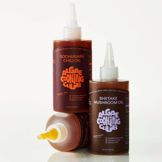 Three bottles of Algae Cooking Club oils including Shiitake Mushroom Oil and Gochugaru Chili Oil displayed together showing product line