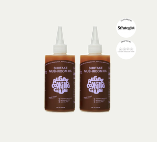 Two bottles of Algae Cooking Club Shiitake Mushroom Oil with brown labels and white caps on beige background, featuring The Strategist logo