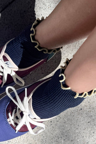 Close-up detail of navy blue sock with contrasting cream wavy ruffle trim at ankle opening