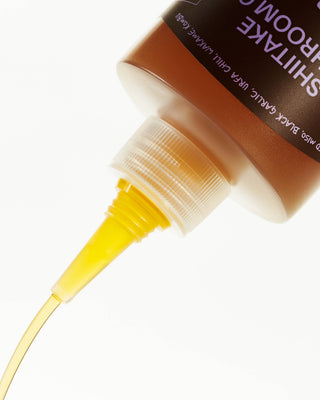 Golden-yellow shiitake mushroom oil being dispensed from squeeze bottle tip in close-up macro shot