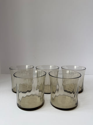 Set of five vintage smoked gray glass tumblers with wavy textured pattern arranged on white surface
