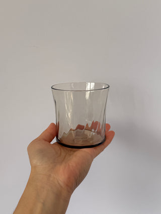 Hand holding single vintage smoked glass tumbler showing gray tint and organic wave texture detail