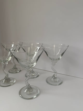 Set of five vintage martini glasses with twisted zig zag stems arranged on white surface, showing classic conical bowls and elegant spiral stems