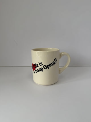Vintage soap opera mug shown from side angle displaying text and cream-colored ceramic finish with handle visible on right