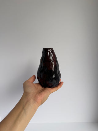 Hand holding vintage aubergine ceramic wabi-sabi vase against white background, showing deep purple-brown glossy glaze and organic textured form
