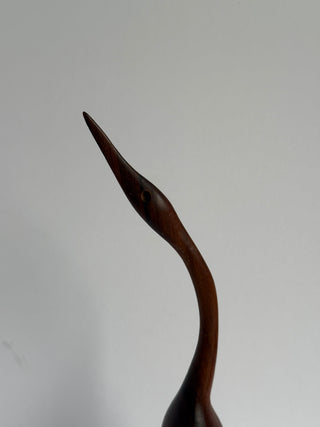 Close-up detail of vintage wooden crane head showing carved eye and pointed beak with wood grain