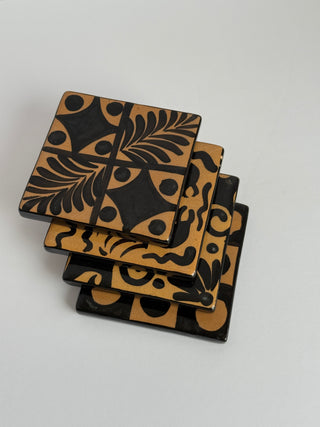 Stacked vintage Honduran coasters at angle showing multiple hand-painted folk art designs including fern, crab, and geometric patterns in black and tan