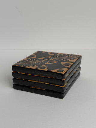 Stack of four vintage Honduran ceramic coasters showing hand-painted fern leaf pattern on top tile with tan and black colors