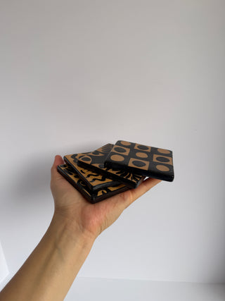 Hand holding stack of vintage Honduran folk art coasters showing thickness and stacked arrangement of decorated ceramic tiles
