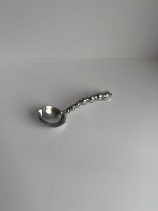 Vintage pewter spoon with spherical beaded handle laying flat on white surface, overhead view