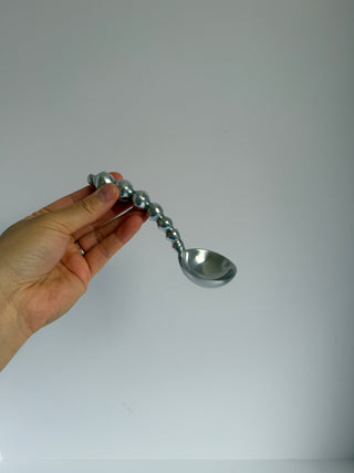 Hand holding vintage silver pewter spoon with graduated beaded handle against white background