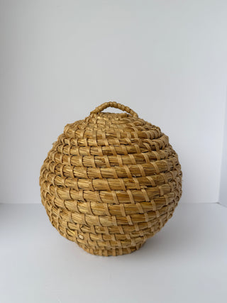 Vintage round woven straw basket with beehive shape and woven handle on top, displayed against white background