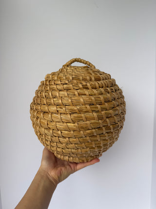 Hand holding vintage round woven basket to show scale, beehive shape with tight woven pattern and handle visible