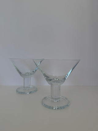 Two vintage martini glasses with wide conical bowls and cylindrical pedestal stems shown at an angle against white background
