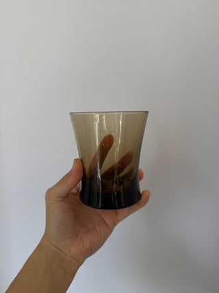 Hand holding vintage smoked umber glass tumbler showing translucent brown gradient glass and dark base detail against white background