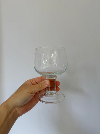 Hand holding single vintage French wine glass showing chunky pedestal stem detail and balloon-shaped clear glass bowl from front angle