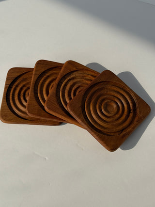 Four vintage teak coasters fanned out showing concentric ring pattern and wood grain detail