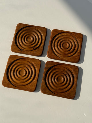 Four vintage teak coasters arranged in grid formation showing matching concentric circle design on each piece