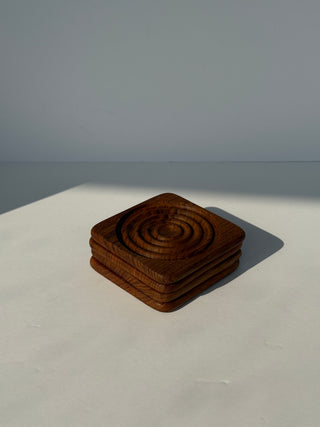 Stack of four vintage teak wood coasters with concentric circle carved design on white surface