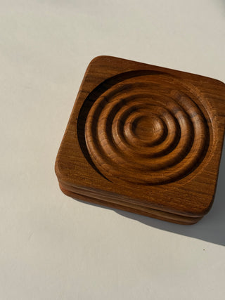 Close-up angle view of stacked vintage teak coasters displaying carved circular grooves and natural wood finish