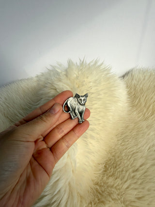 Hand holding vintage Rawcliffe pewter cat brooch to show size scale against cream fur background