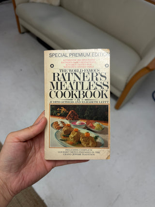 Front cover of vintage Ratner's Meatless Cookbook Special Premium Edition with cream colored paperback showing food photography of dairy dishes on table