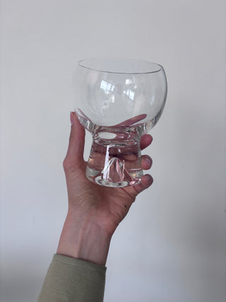 Side view of vintage clear glass goblet with twisted sculptural stem held in hand against white background