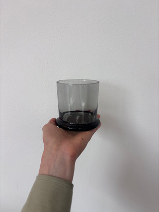 Vintage smoked glass tumbler with black base held in hand against white background, side view