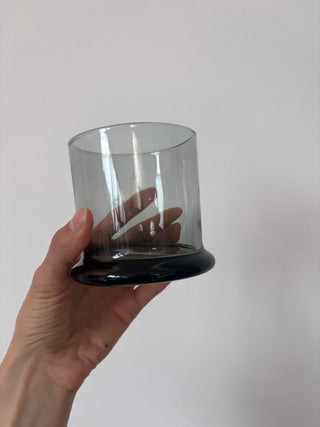 Side angle of vintage smoked glass tumbler held in hand showing transparent gray body and black base