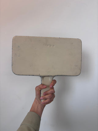 Bottom view of vintage enamelware tray showing maker's mark and handle, held against white background