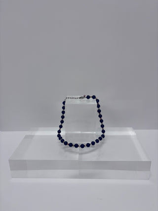 Vintage lapis blue beaded necklace displayed on white acrylic jewelry stand against neutral background