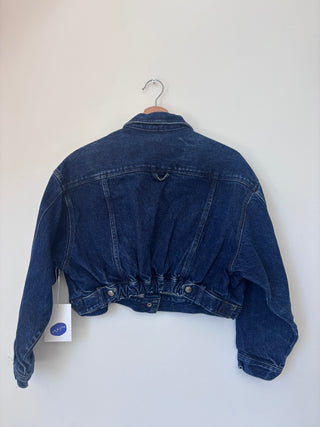 Back view of vintage cropped denim jacket displaying gathered waist with adjustable snap tabs and structured collar detail