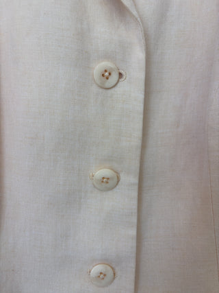 Detail view of cream colored buttons on beige linen vest showing buttonhole finishing and fabric texture