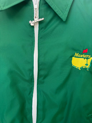 Close-up detail of Masters logo embroidery with yellow map and red flag, Cadmaster zipper pull visible on green nylon fabric
