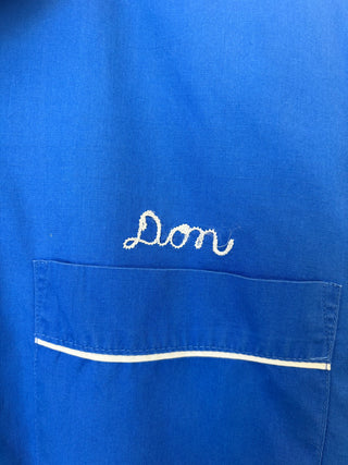 Detail shot of white chain-stitch embroidered name 'Don' above chest pocket on royal blue fabric