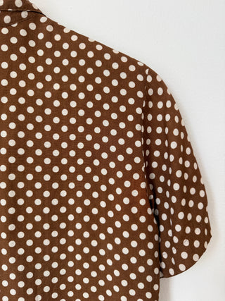 Detail shot of brown rayon fabric with cream polka dots showing texture and short sleeve construction