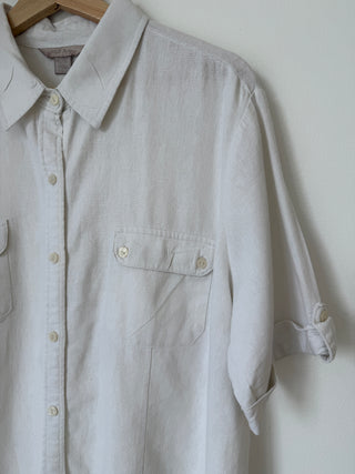 Close-up detail of vintage cream linen shirt showing button-flap chest pocket, rolled sleeve detail, and natural linen texture