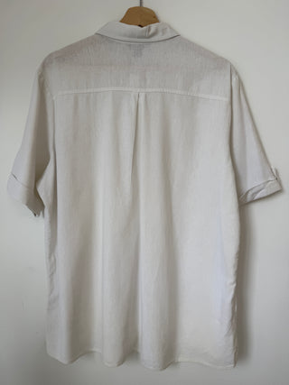 Full back view of vintage cream linen button-up shirt on wooden hanger showing relaxed silhouette and roll-tab sleeve styling