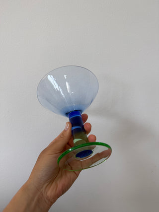 Bottom angle view of vintage art glass martini coupe held upside down, displaying the green circular base and ridged multicolor stem construction