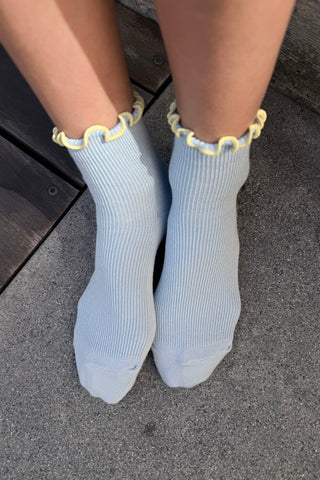 Overhead view of feet wearing light blue ribbed socks with yellow ruffled trim and colorblock canvas sneakers